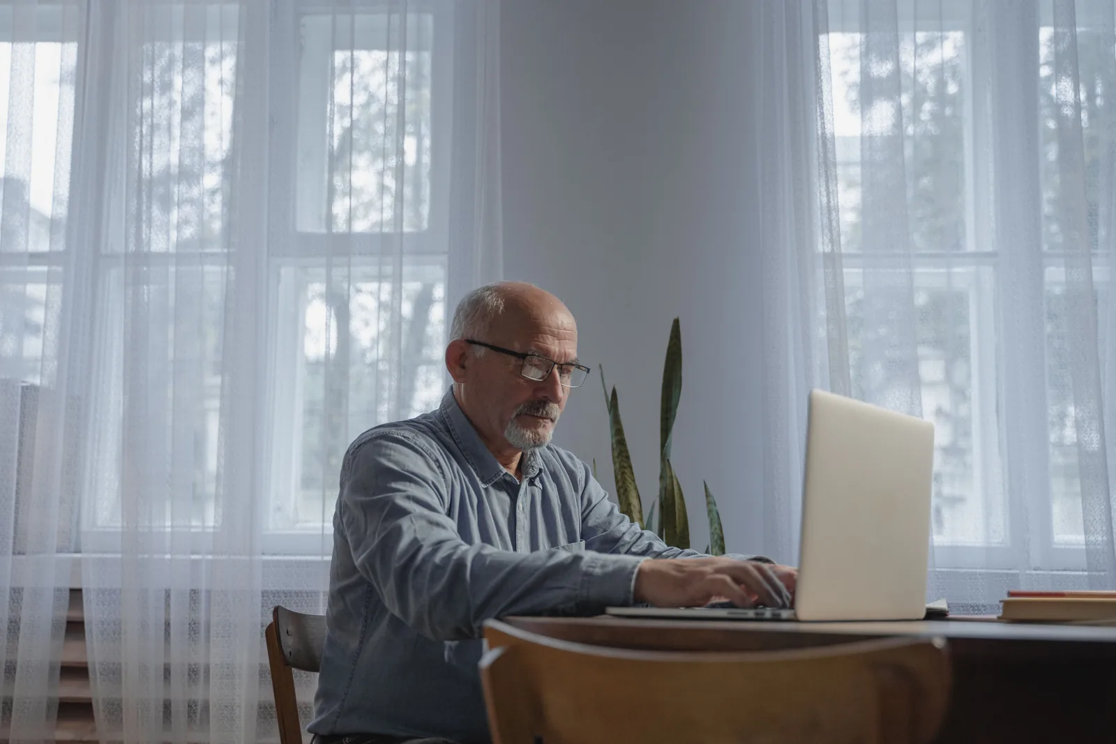 Ein älterer Mann arbeitet zu Hause konzentriert an seinem Laptop.